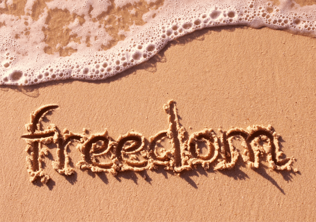 Sandstrand mit "Freedom" Schriftzug und Wellen im Meer